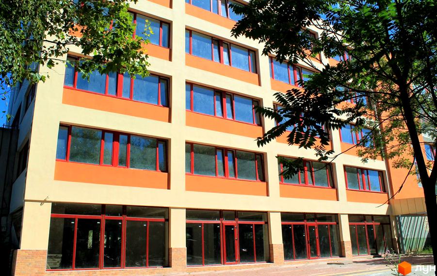 Фасад житлового комплексу Тираспольський з великими вікнами та червоними рамами. Будинок має помаранчеві та світло-бежеві елементи. Навколо будівлі зелені дерева.