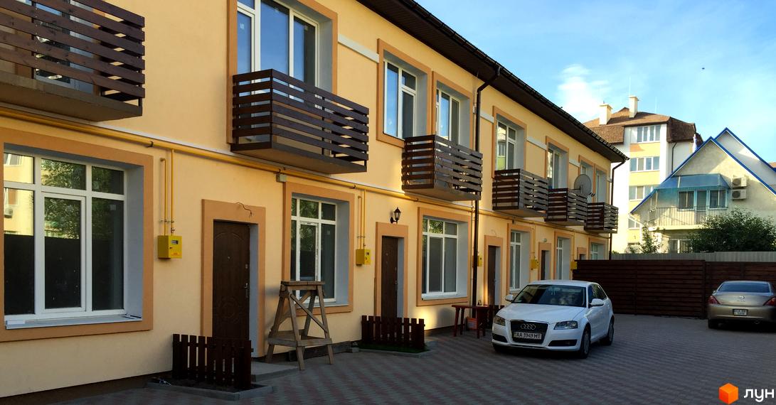 Зовнішній вигляд житлового комплексу Таунхауси „Родинний“ з балконами та вікнами. На прибудинковій території розташовані автомобілі та парковка.