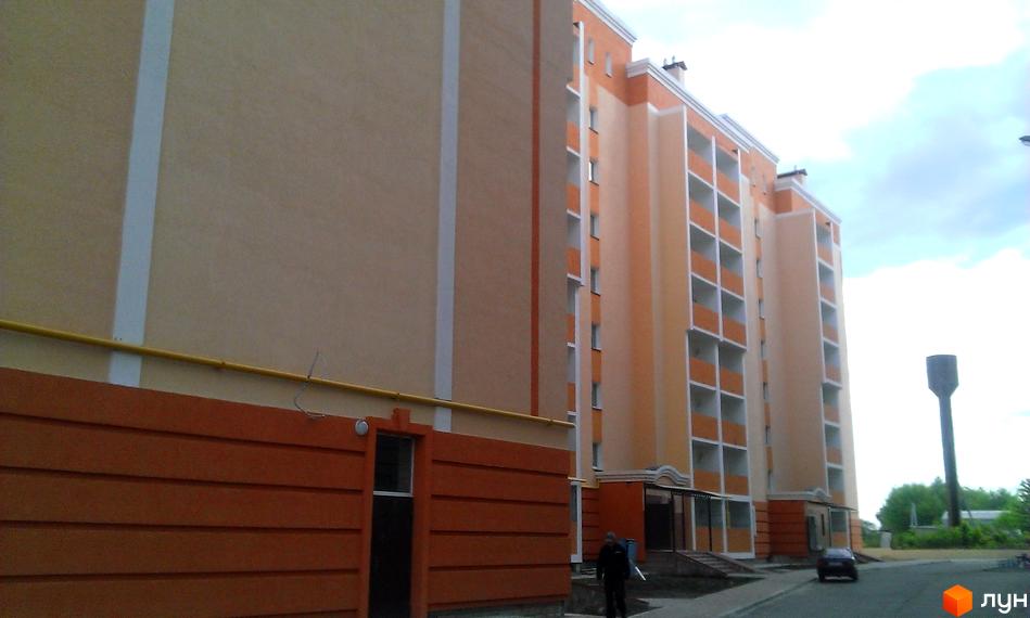 Зображення фасаду та прибудинкової території Житлового комплексу Новокиївський. Багатоповерхова будівля з балконами та парковкою.