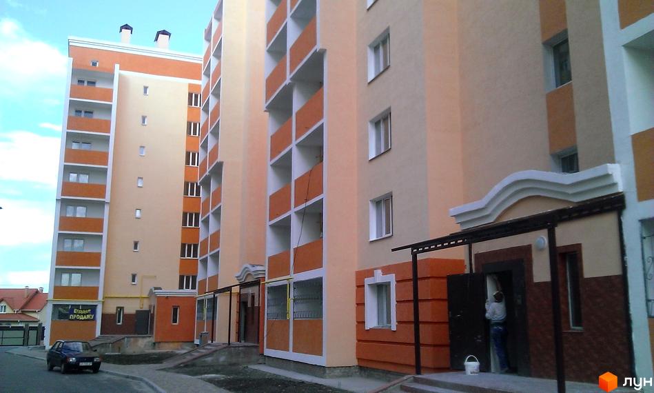 Зображення фасаду та прибудинкової території Житлового комплексу Новокиївський. Багатоповерховий будинок з балконами та вікнами.