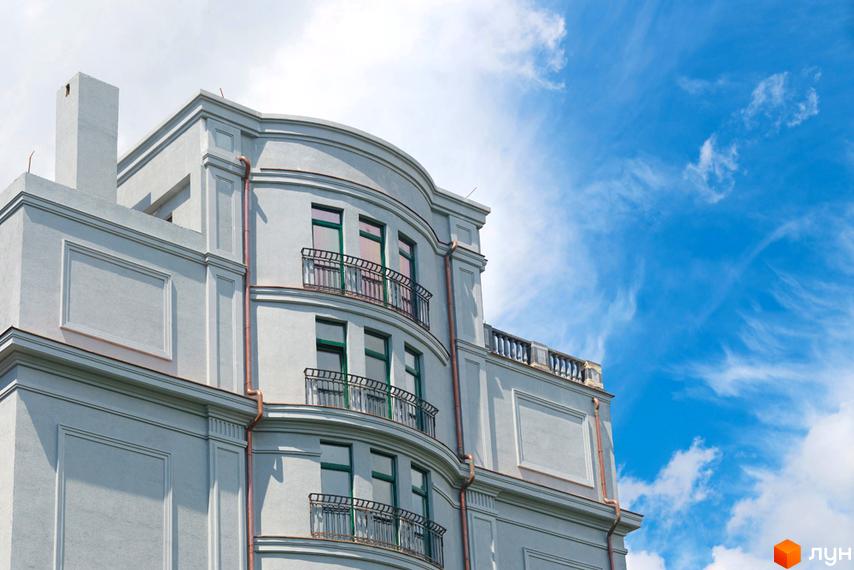 Фасад житлового комплексу ЖК Зелена тераса з балконами та вікнами на тлі блакитного неба з хмарами. Архітектура будівлі має витончені вигини та декоративні елементи.