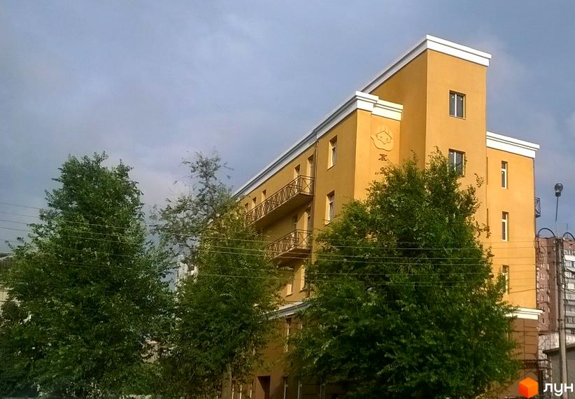 Житловий комплекс по пров. Мовчанівський, 31. Жовта будівля з балконами та білими обрамленнями. На передньому плані зелені дерева.