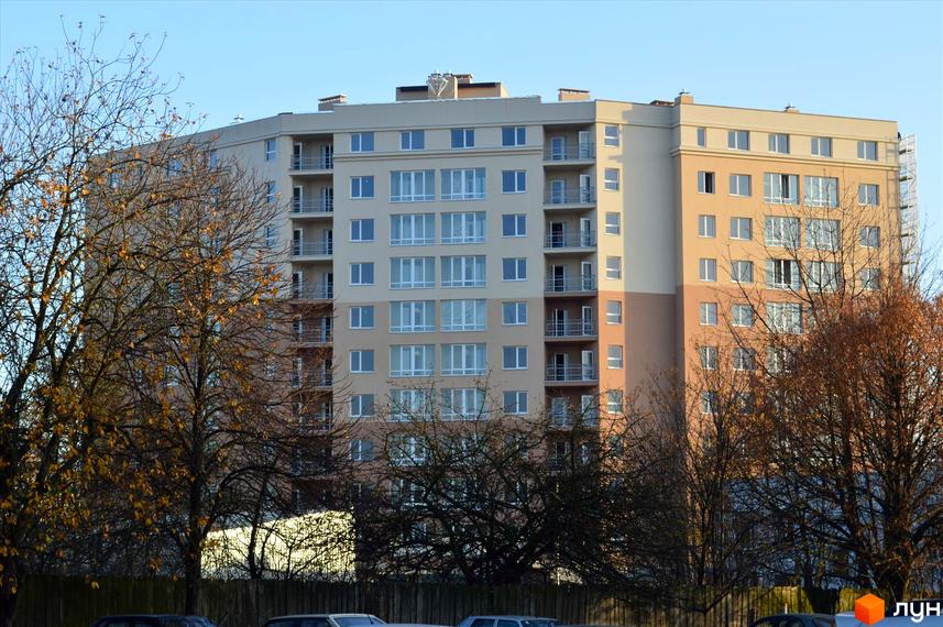 Зовнішній вигляд житлового комплексу Ювелірний з численними вікнами та балконами. Навколо будівлі видно дерева та паркан.