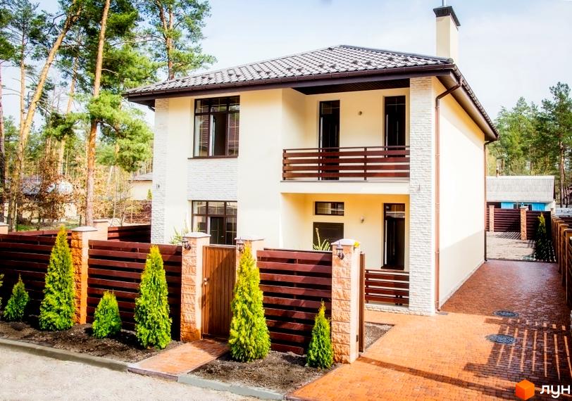 Двоповерховий будинок з балконом та коричневим парканом. На прибудинковій території висаджені туї, доріжка викладена бруківкою.