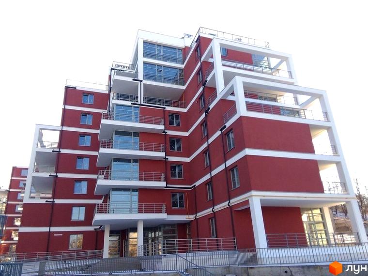 Зображення фасаду Новобудови Золотий горіх з балконами. Багатоповерхова будівля з червоними стінами та білими балконами.