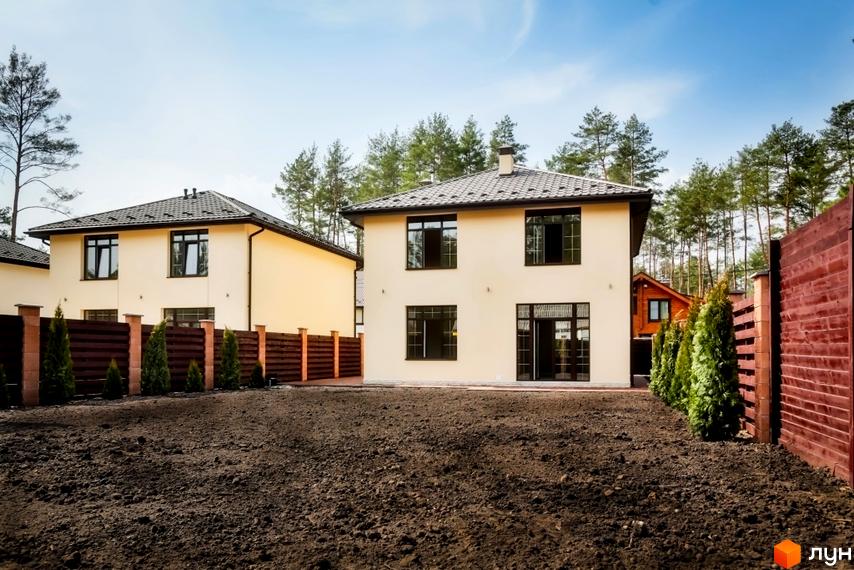 Двоповерховий будинок з великими вікнами та темним дахом. Перед будинком – необладнана ділянка, огороджена дерев'яним парканом.