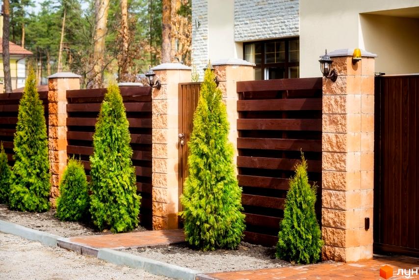 Котеджне містечко КМ Твій Дім. Огорожа з цегляних стовпів та дерев'яних ламелей з туями біля будинку. Прибудинкова територія з доріжками.