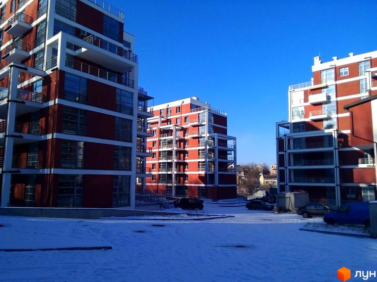 Зображення фасаду та прибудинкової території Житлового комплексу Золотий горіх. На фото декілька багатоповерхівок з червоною обробкою та білими балконами.