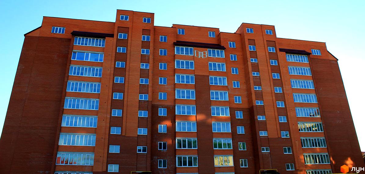 Зовнішній вигляд цегляної новобудови з численними вікнами. Будинок має багатоповерхову структуру з різними секціями.