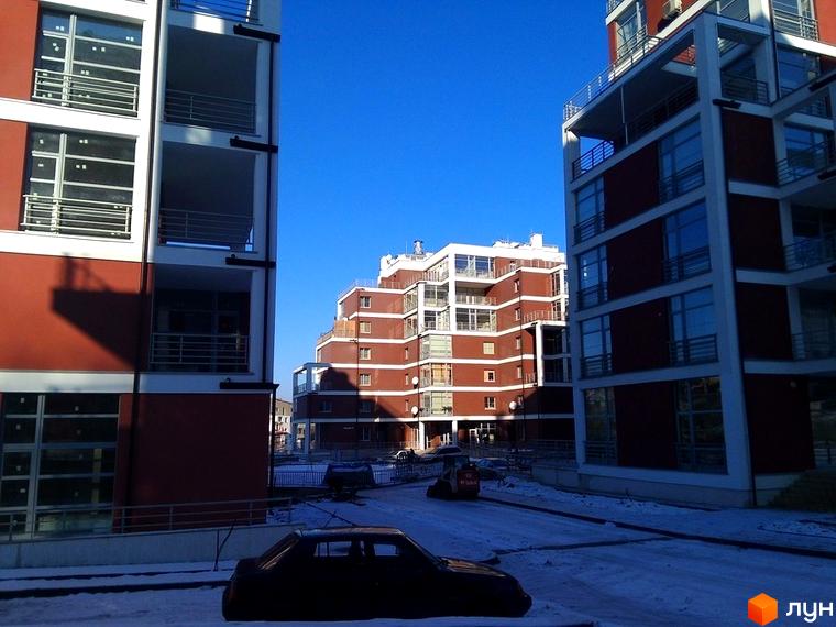 Зображення житлового комплексу Золотий горіх. Багатоповерховий будинок з червоною цеглою та білими балконами. Навколо сніг та припарковані автомобілі.