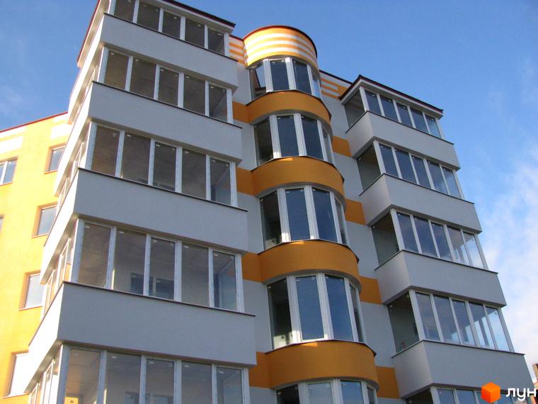 Багатоповерховий будинок ЖК Приозерний з великими вікнами та балконами. Фасад будівлі виконаний у сіро-жовтих кольорах, видно блакитне небо.