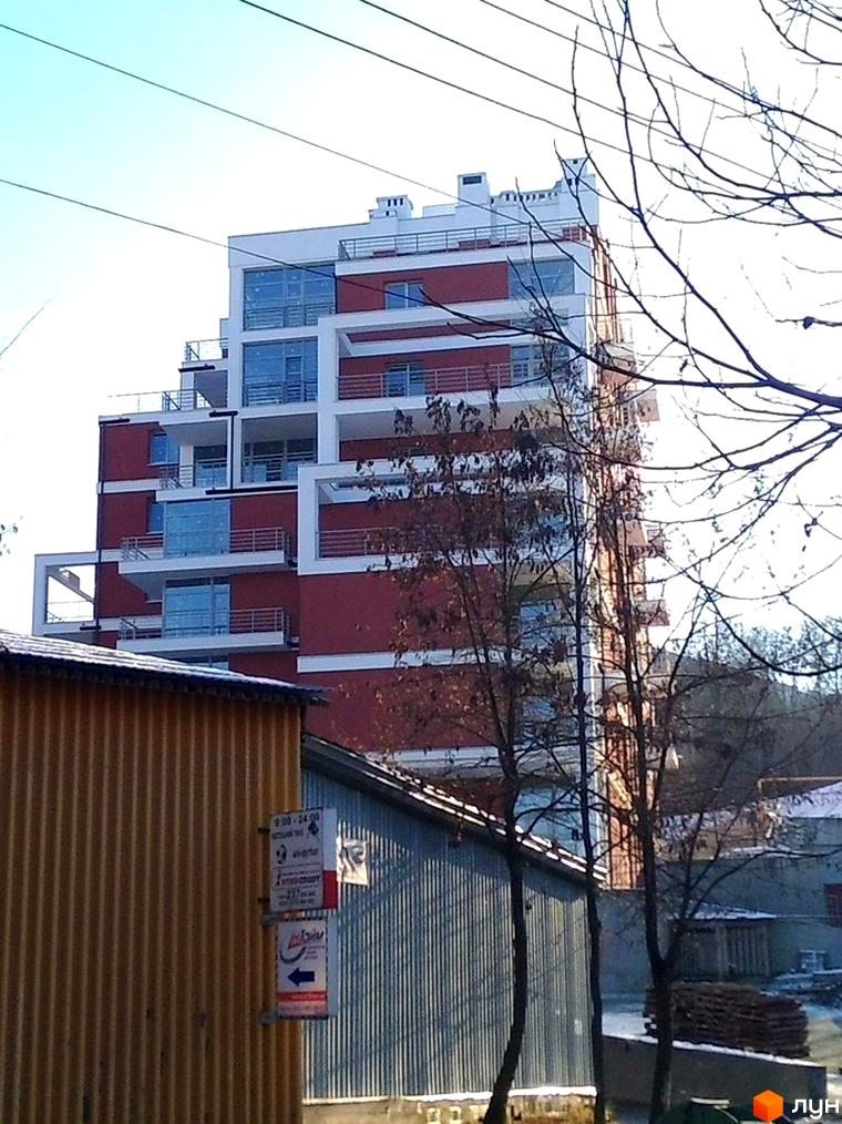 Зовнішній вигляд багатоповерхового будинку з балконами. Житловий комплекс Золотий горіх на фоні дерев та будівель.