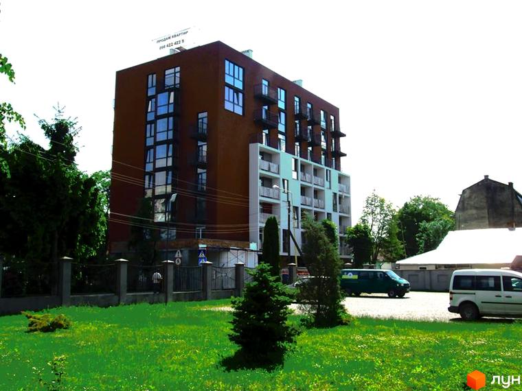Багатоповерховий будинок з балконами та великими вікнами. На передньому плані зелена галявина з деревами та кущами.