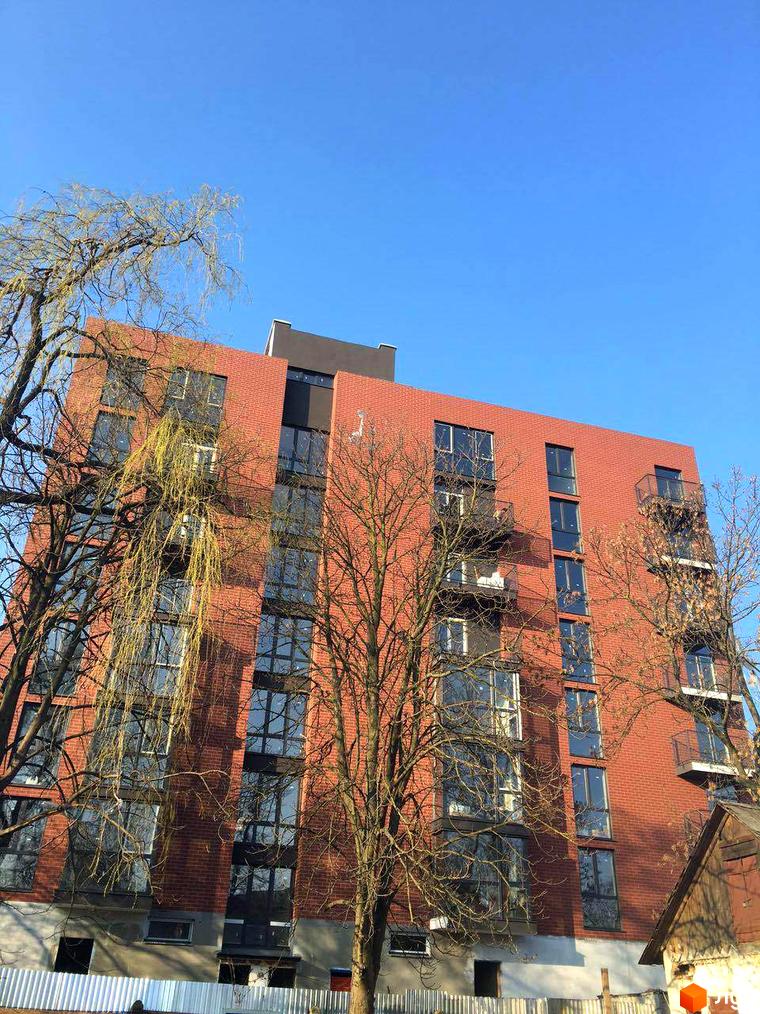 Новобудова на вулиці Дубравського, 5 з червоної цегли та великими вікнами. Навколо будівлі ростуть дерева без листя.