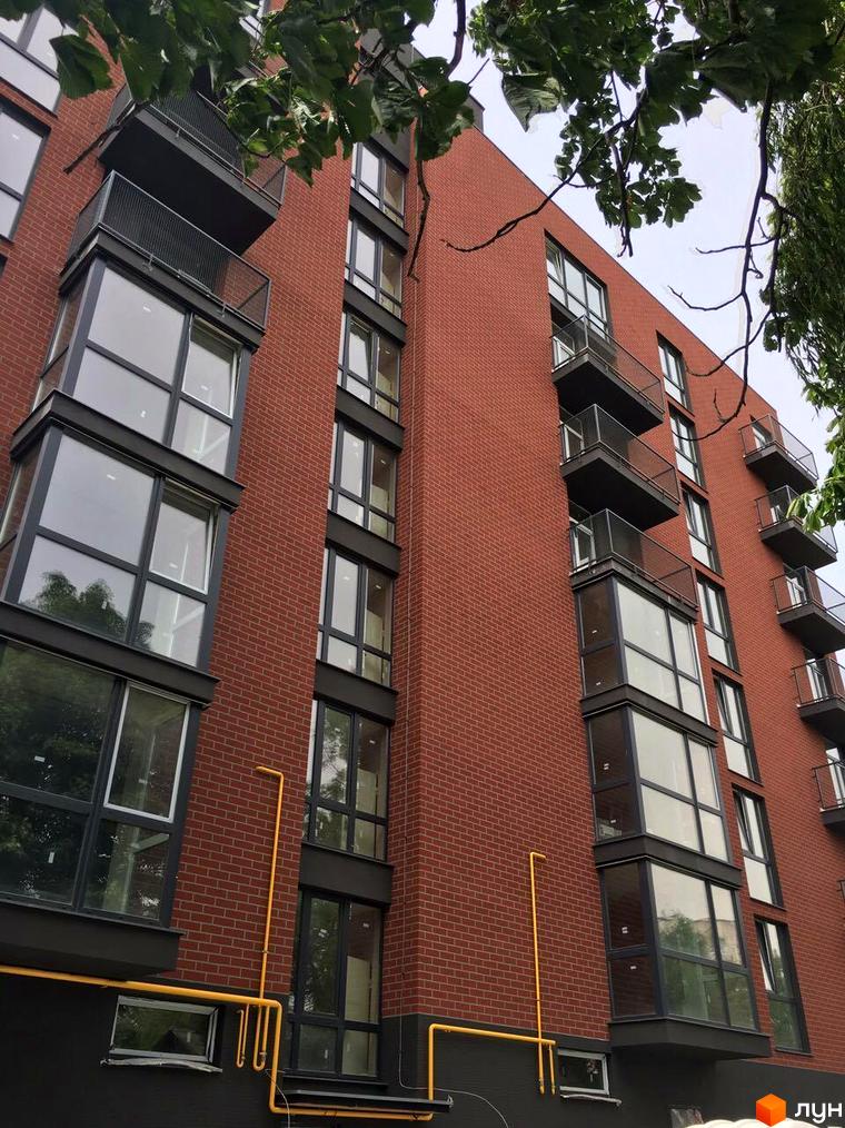 Високий будинок з червоної цегли з великими вікнами та балконами. ЖК на вул. Дубравського, 5.