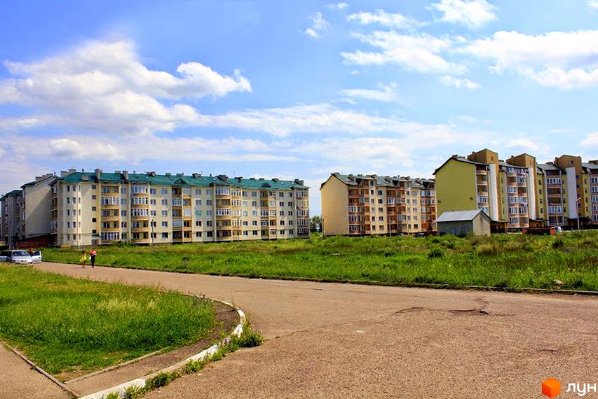 Житловий комплекс на вул. Об'їздна. Багатоповерхові будинки з зеленими дахами розташовані серед зеленої трави та асфальтованої дороги. На фоні блакитне небо з хмарами.