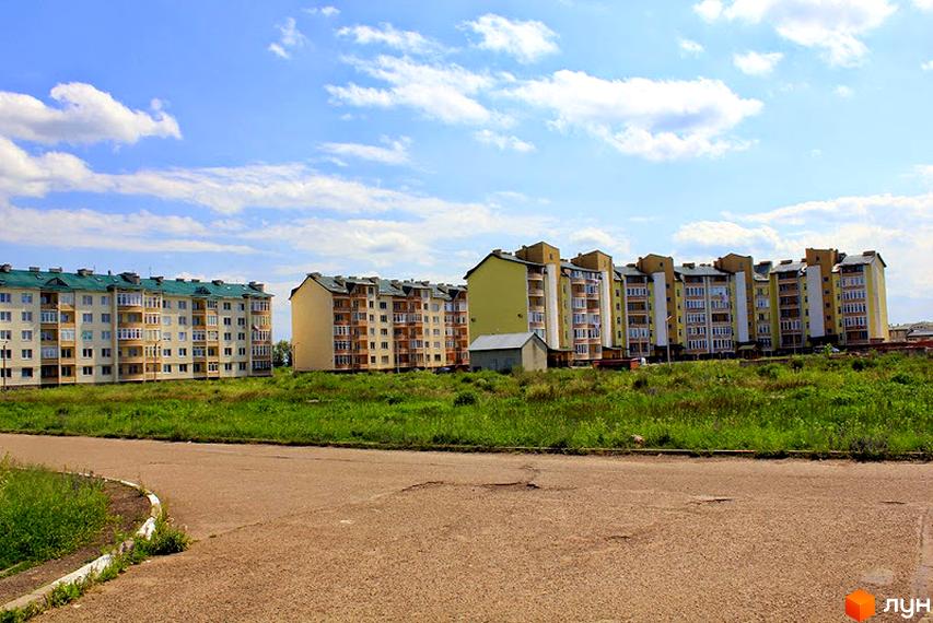 Зовнішній вигляд житлового комплексу на вулиці Об'їзній: багатоповерхові будинки з зеленими дахами та балконами. Навколо новобудов - зелена територія з травою та дорогою.