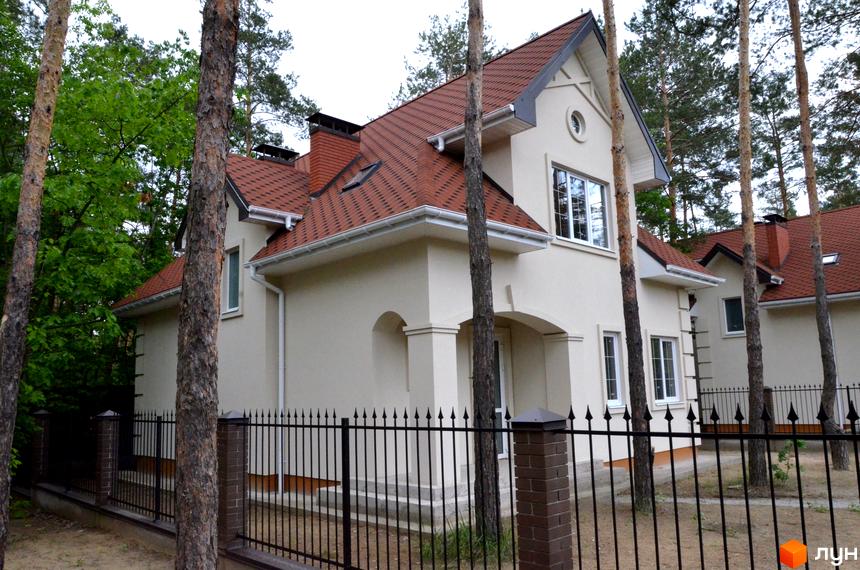 Фото будинку в Житловому комплексі AlpenPark з червоною черепицею та білим фасадом. Навколо сосни та чорна огорожа.