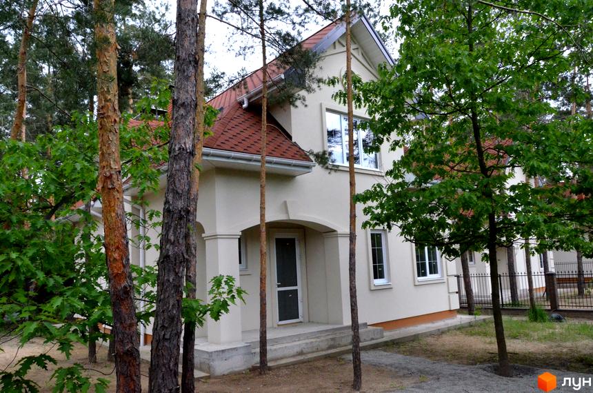 Зображення будинку в Житловому комплексі AlpenPark з червоним дахом та білими стінами, оточеного деревами. Навколо будинку зелена прибудинкова територія.