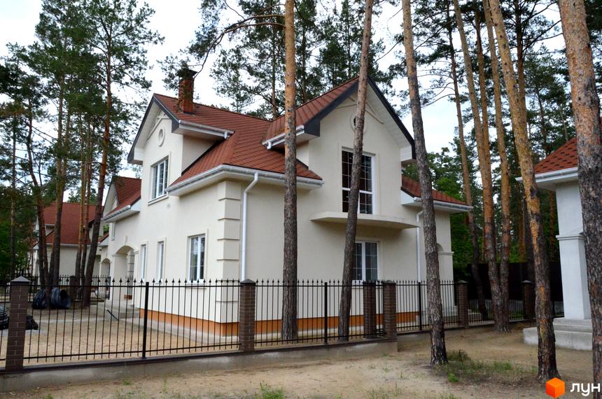 Резиденція AlpenPark: двоповерхові будинки з червоним дахом та білими фасадами, оточені високими соснами. Огороджена територія з кованим парканом та цегляними стовпами.