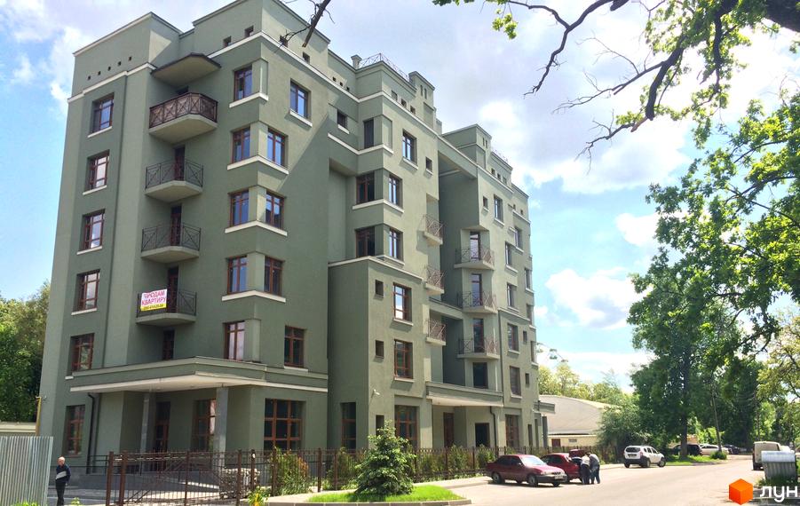 Зовнішній вигляд клубного будинку Парковий з балконами та вікнами. Навколо будинку дерева та дорога з автомобілями.