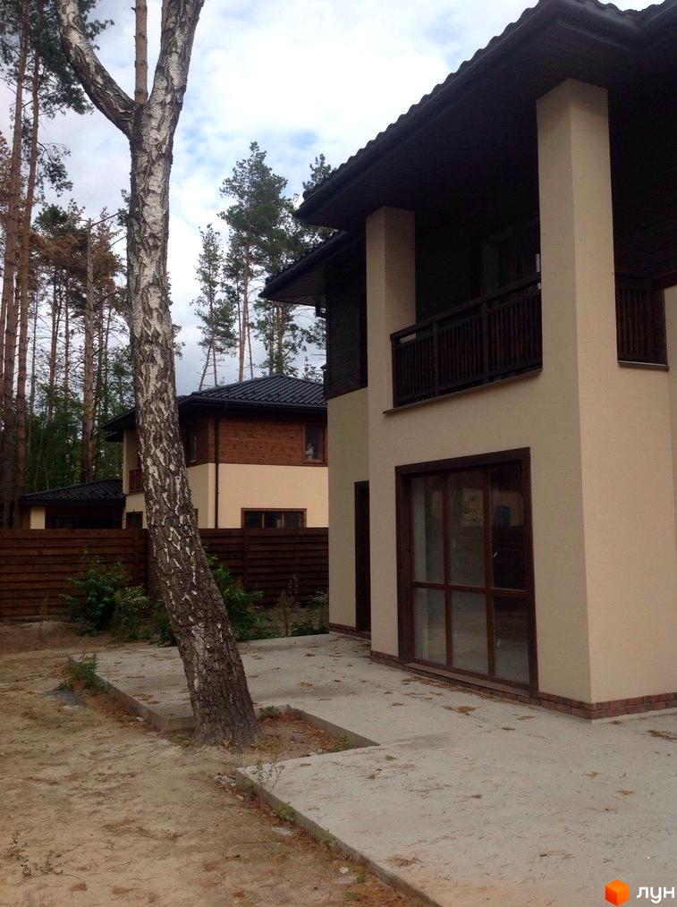Котеджне містечко Forest Family Avenue. Зовнішній вигляд двоповерхових будинків з дерев'яними та світлими фасадами, огороджених дерев'яним парканом. Навколо будівель ростуть високі дерева.