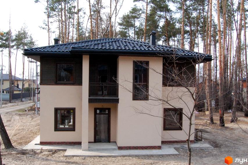 Котеджне містечко Forest Family Avenue: двоповерховий будинок з темним дахом та коричневими вікнами, розташований серед високих сосен. Навколо будинку піщана ділянка та дорога.