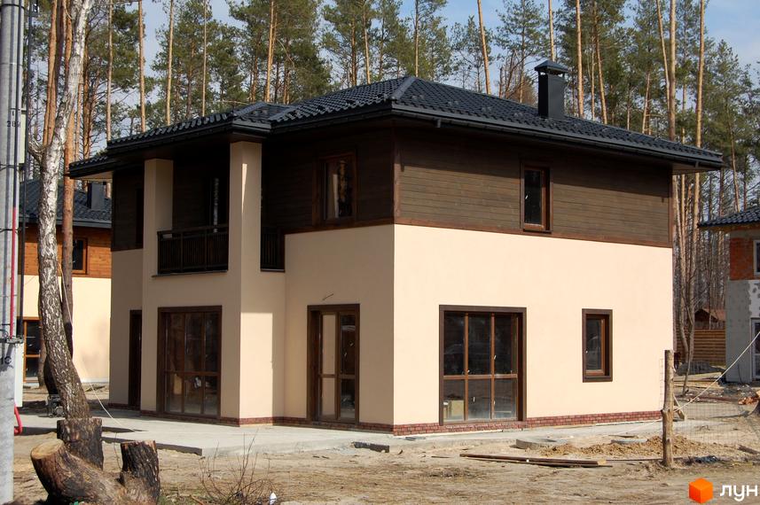 Котеджне містечко Forest Family Avenue: двоповерховий будинок з бежевим фасадом та коричневими дерев'яними елементами, великими вікнами та темним дахом. Навколо будинку - ліс та будівельний майданчик.