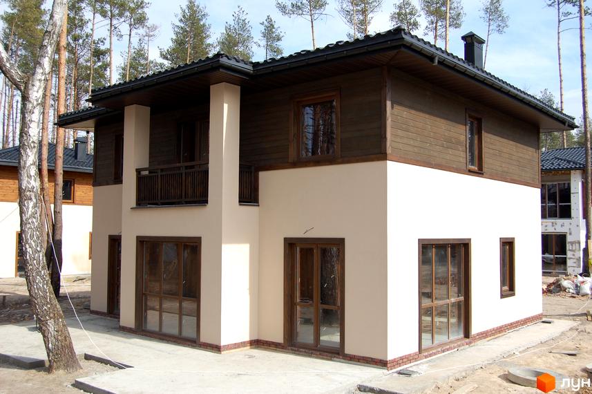 Котеджне містечко Forest Family Avenue. Двоповерховий будинок з дерев'яним оздобленням фасаду та великими вікнами. Навколо будинку - ліс та будівельні роботи.