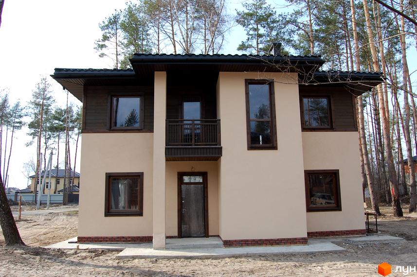 Котеджне містечко Forest Family Avenue: двоповерховий будинок з коричневими вікнами та темним дахом, розташований серед соснового лісу. Навколо будинку піщана ділянка та зелені насадження.