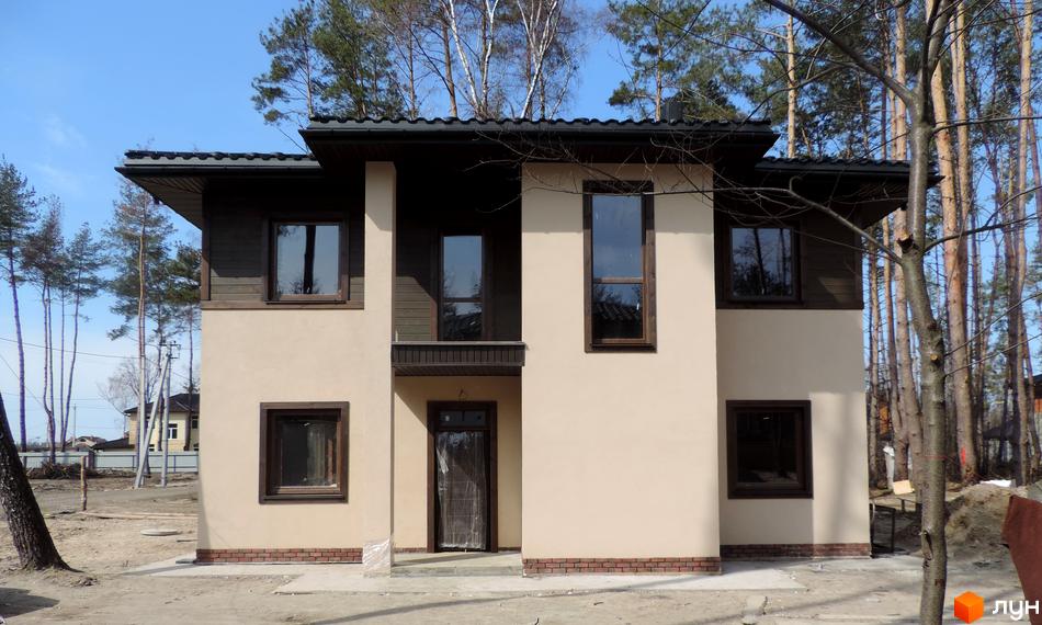 Котеджне містечко КМ Forest Family Avenue. Зовнішній вигляд двоповерхового будинку з коричневими вікнами та темно-коричневим дахом. Навколо будинку дерева та ділянка з будматеріалами.