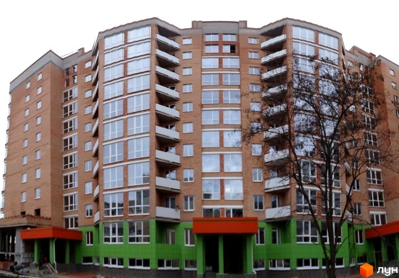 Зовнішній вигляд новобудови ЖК Адмірал Сенявін з цегляним фасадом та великими вікнами. Будинок має багатоповерхову структуру з балконами та зеленим оздобленням нижньої частини.