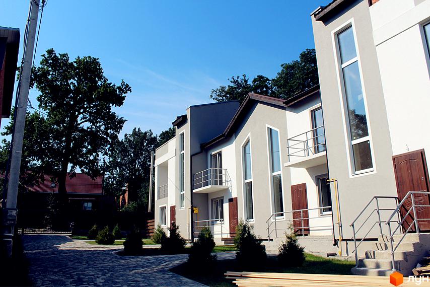 Таунхаус „Емірати“: будинки світлих відтінків з великими вікнами та балконами. Навколо – вимощена доріжка, зелені кущі та дерева.