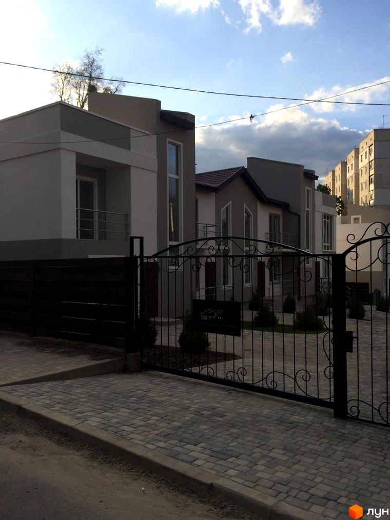 Таунхаус „Емірати“: ряд будинків з світло-сірими та темно-сірими фасадами, великими вікнами та балконами. Перед будинками кована огорожа та бруківка.