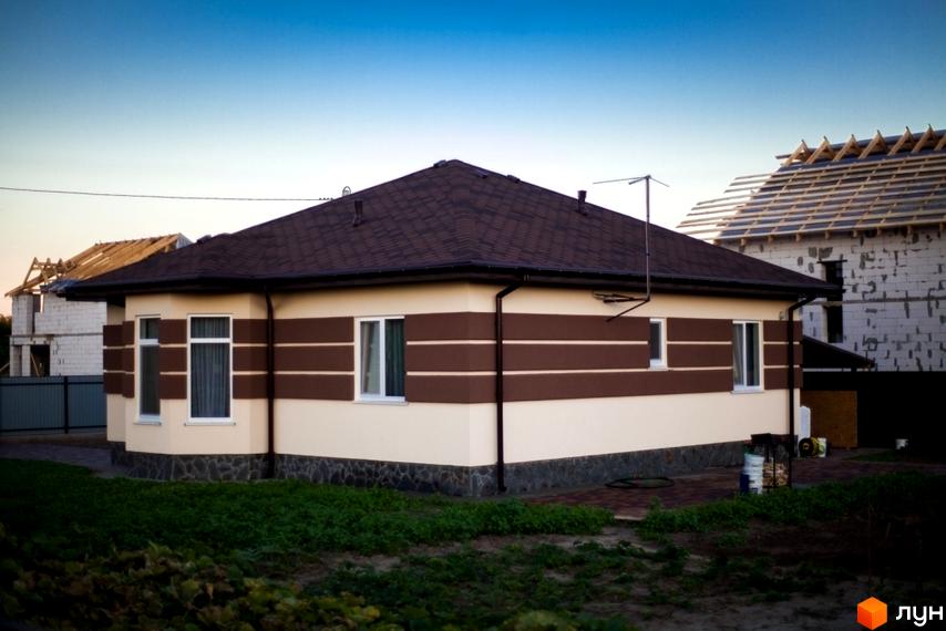 Одноповерховий будинок у Котеджному містечку HappyTown з коричневим дахом та бежевими стінами з горизонтальними коричневими смугами. Прибудинкова територія з зеленою травою.