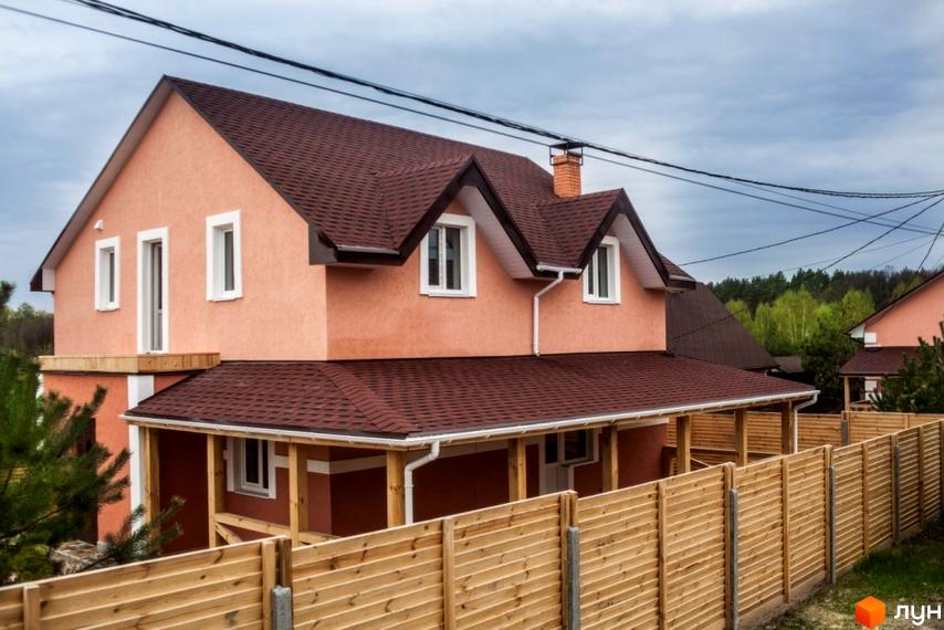 Двоповерховий будинок персикового кольору з темно-коричневим дахом та білими вікнами. Перед будинком розташований дерев'яний паркан Котеджне містечко HappyTown.