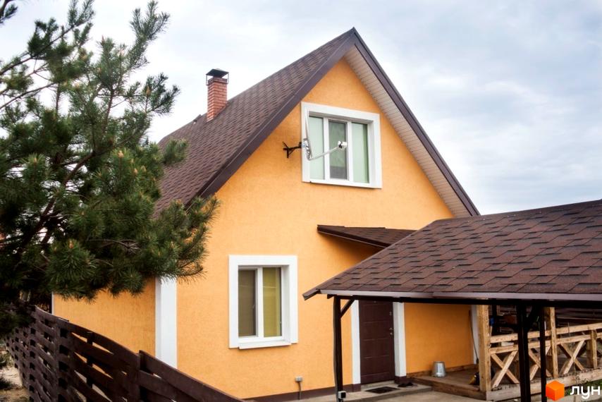 Помаранчевий будинок Котеджного містечка HappyTown з коричневим дахом та білими вікнами. На території видно дерев'яний паркан та криту терасу.