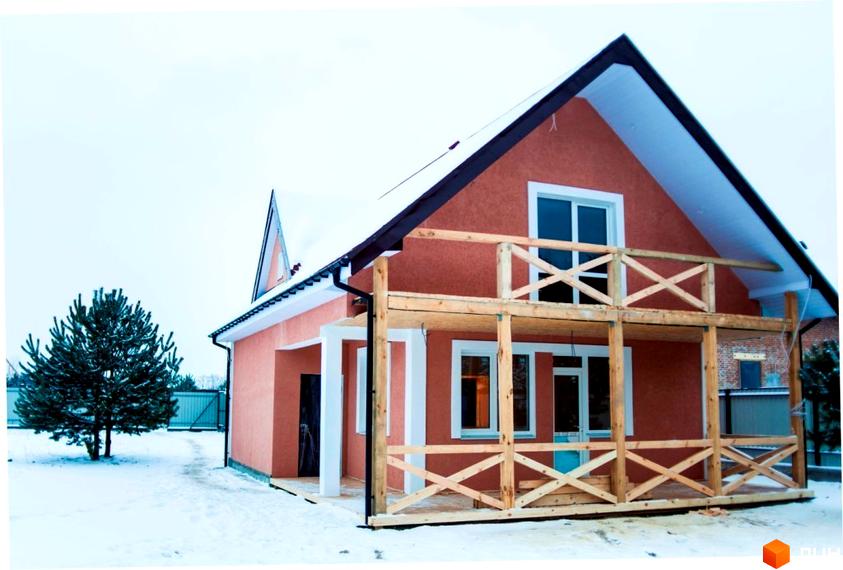 Двоповерховий будинок Котеджного містечка HappyTown з помаранчевим фасадом, білими вікнами та дерев'яною терасою. Розташований на засніженій ділянці з сосною.