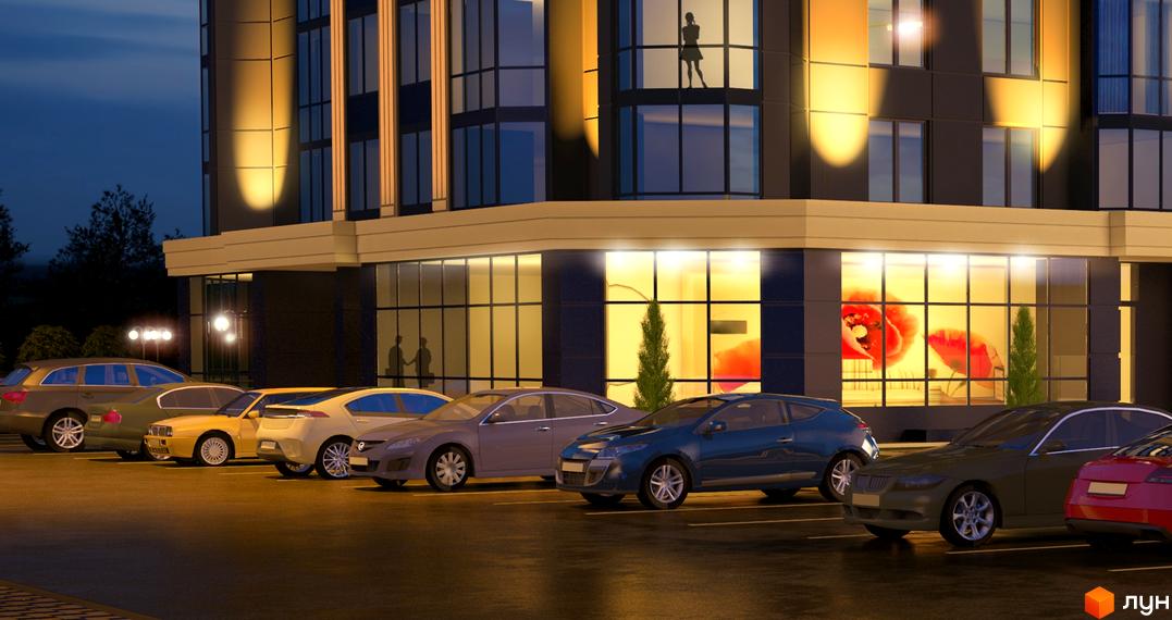 Житловий комплекс Sky ввечері з освітленими вікнами та скляним фасадом на першому поверсі. Перед будинком розташований паркінг з автомобілями.