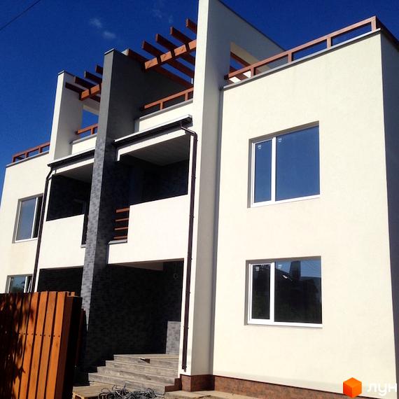 Фасад будинку Котеджного містечка High-Tech House зі світлими стінами, темними акцентами та дерев'яними перголами на даху.