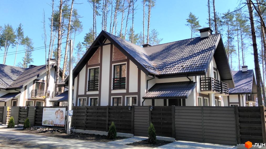 Зображення житлового будинку в Котеджному містечку Едельвейс. Будинок має двосхилий дах, білі стіни з коричневими елементами та дерев'яний паркан навколо території.