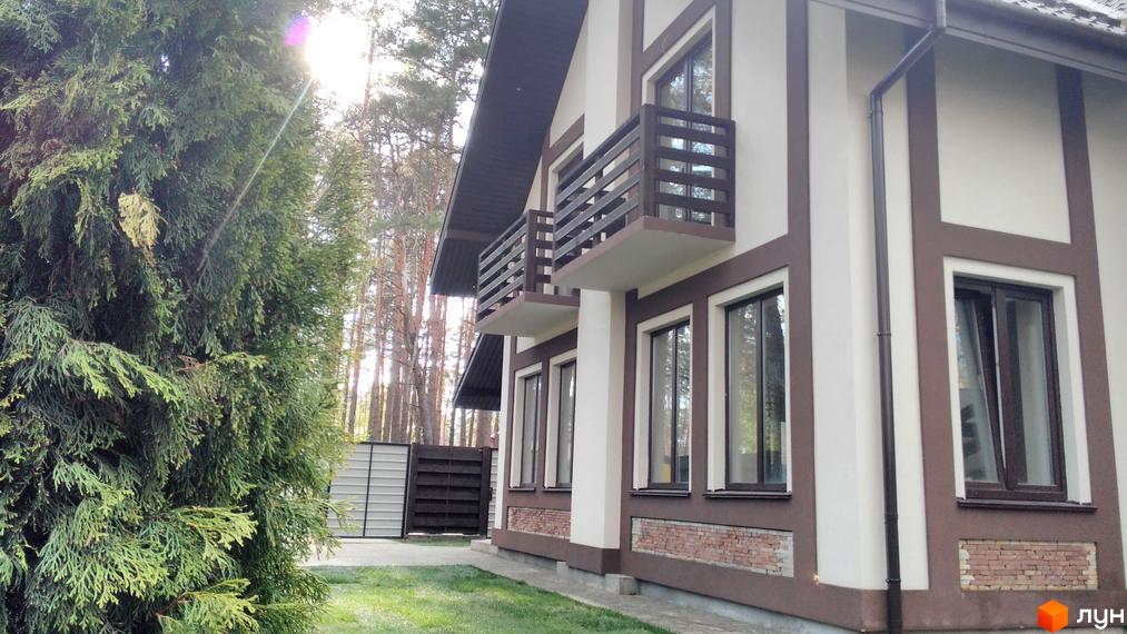 Зображення двоповерхового будинку в Котеджному містечку Едельвейс. Вигляд фасаду з балконами та вікнами, зелена галявина перед будинком.