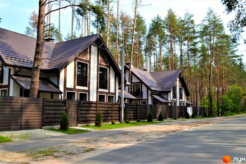 Зображення житлового комплексу Едельвейс. На фото видно будинки з коричневою черепицею та білими стінами. Перед будинками розташований дерев'яний паркан та зелені насадження.