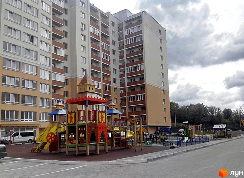 Зображення фасаду будинку на Лісогринівецькій, 26/3, 28, 30/3, 30/4. На передньому плані дитячий майданчик з гірками та гойдалками.