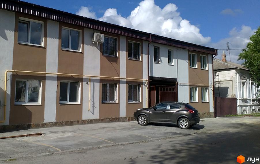 Будинок ЖК Одеський дворик з коричнево-білими смугами та кондиціонером. Перед будинком парковка з сірим автомобілем.
