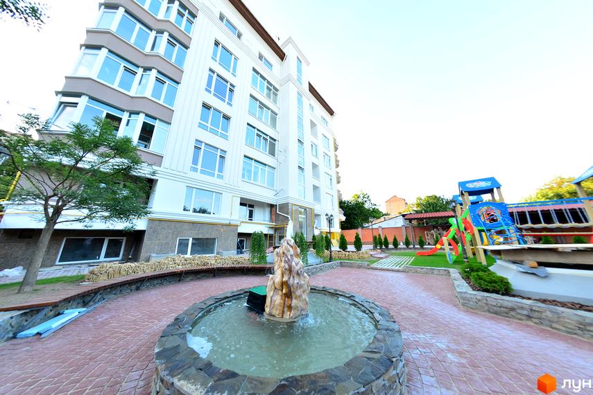 Новобудова на вулиці Мала Морська, 2а, з фасадом білого кольору та великою кількістю вікон. На прибудинковій території розташовані дитячий майданчик та фонтан.