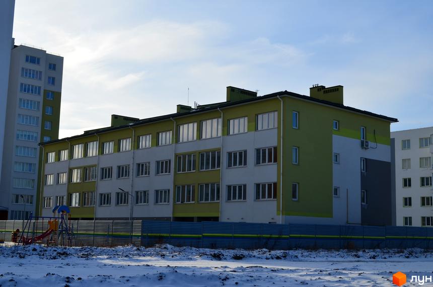 Зображення фасаду будинку у Житловому районі Новий. На передньому плані видно дитячий майданчик та сніг.