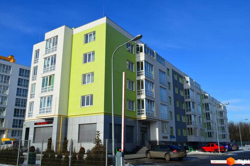 Зображення фасаду та прибудинкової території Житлового комплексу Новий. Багатоповерховий будинок з великими вікнами та парковкою.