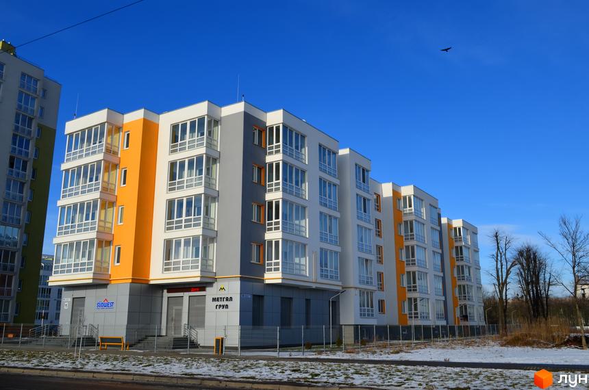 Зображення фасаду житлового комплексу Новий. Багатоповерхова будівля з великими вікнами та кольоровими вставками на фоні блакитного неба.