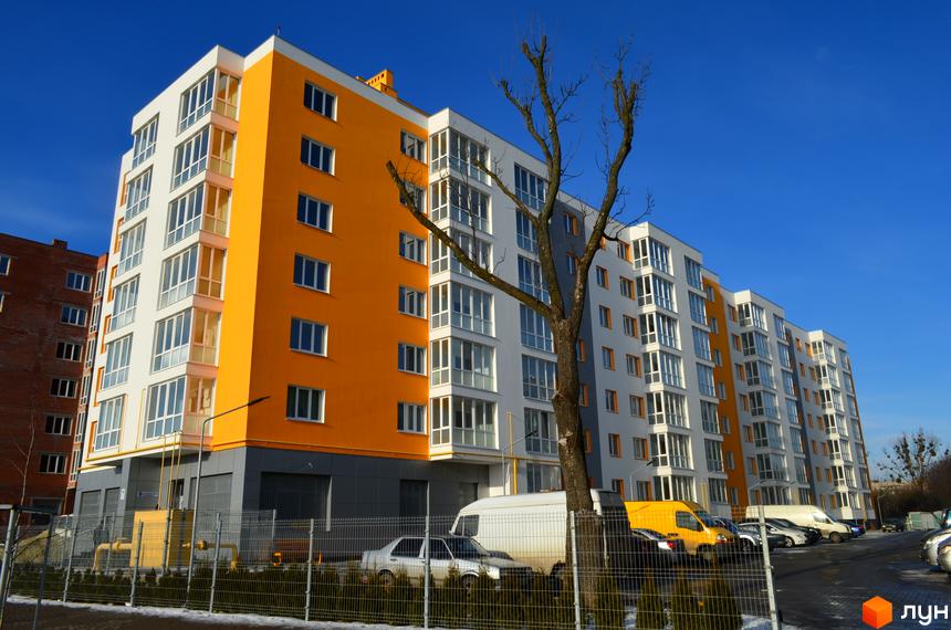 Зовнішній вигляд багатоповерхового будинку в Житловому комплексі Новий. На передньому плані прибудинкова територія з деревами та парковкою.